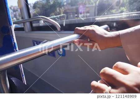 Close-up of Hands Holding Bus Rail in Sunny Public Transport Close-up of Hands Holding Bus Rail in Sunny Public Transport 121148909