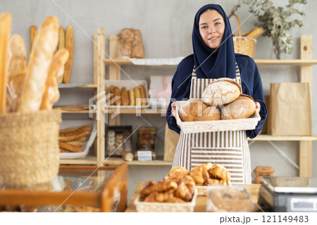 Portrait of girl seller of oriental bakery in traditional Muslim clothes with of baguettes Portrait of girl seller of oriental bakery in traditional Muslim clothes with of baguettes 121149483