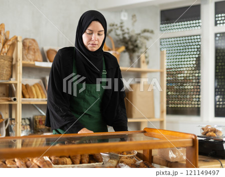 Saleswoman in a hijab collects pastries in a container Saleswoman in a hijab collects pastries in a container 121149497