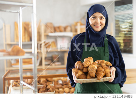 Middle-aged Muslim saleswoman displays croissants in wicker basket Middle-aged Muslim saleswoman displays croissants in wicker basket 121149499