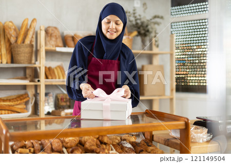 Saleswoman in a hijab holds a box with a bow Saleswoman in a hijab holds a box with a bow 121149504