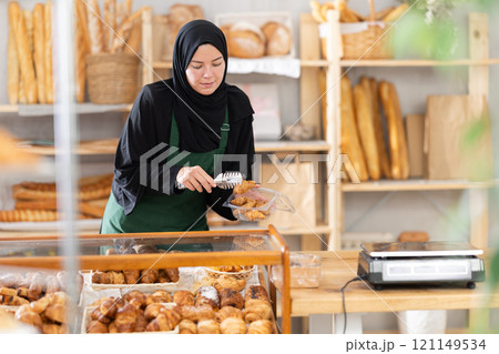 Girl seller of an oriental bakery in traditional muslim clothes with fresh hot croissants in hands Girl seller of an oriental bakery in traditional muslim clothes with fresh hot croissants in hands 121149534