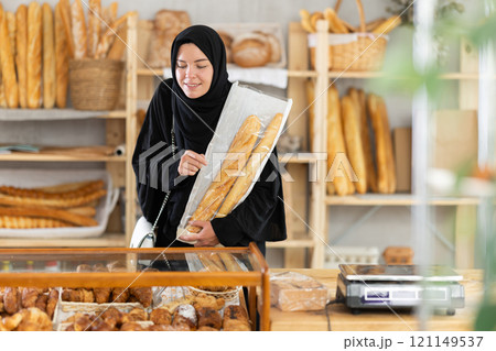 Young woman in Muslim clothing choosing pastries in bakery 121149537