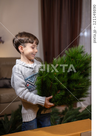 Young caucasian boy holding christmas tree indoors. 121149890