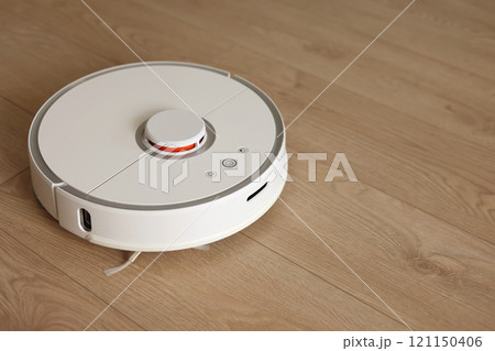 Top view of white wireless autonomous robotic vacuum cleaner on wooden floor. Smart cleaning technology. Self-propelled cleaning robot. Floor cleaning system. Household remote control appliances. 121150406