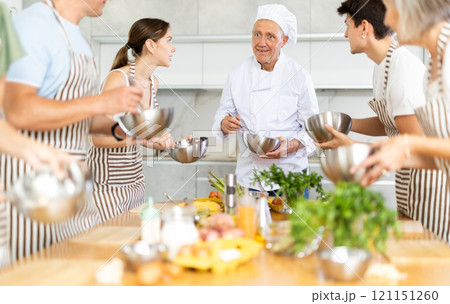 Smiling old man chef of cooking course teaching attendees how to mix sauce 121151260