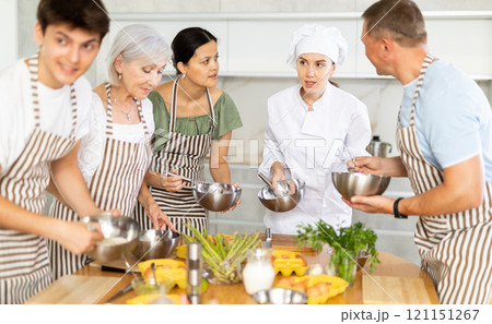 Young female cook teaches to cook group of people Young female cook teaches to cook group of people 121151267
