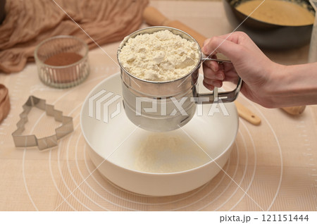 Christmas homemade baking, ingredients for baking gingerbread, woman sifting flour in a white bowl 121151444
