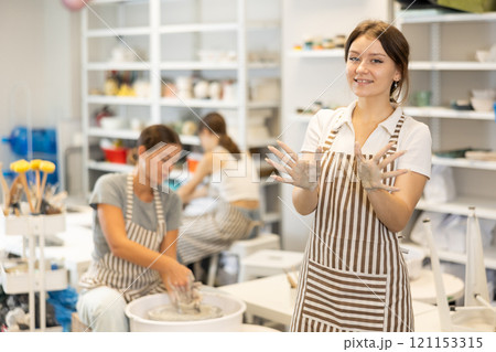 Girl takes break, stands and rests, waves hello with her hands stained with clay during pottery class 121153315