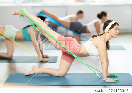 Young girl practicing back leg lift with band standing on knees Young girl practicing back leg lift with band standing on knees 121153348