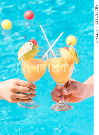 バカンス・リゾートホテルのプールサイドでトロピカルドリンクで乾杯するカップルの手元 バカンス・リゾートホテルのプールサイドでトロピカルドリンクで乾杯するカップルの手元 121153598
