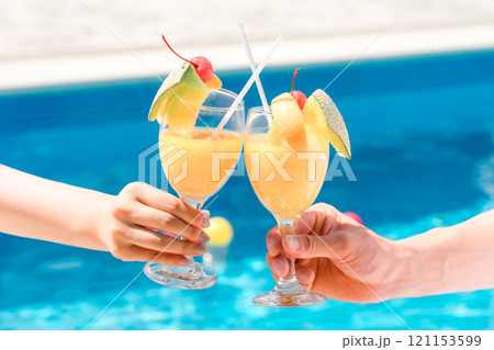 バカンス・リゾートホテルのプールサイドでトロピカルドリンクで乾杯するカップルの手元 バカンス・リゾートホテルのプールサイドでトロピカルドリンクで乾杯するカップルの手元 121153599