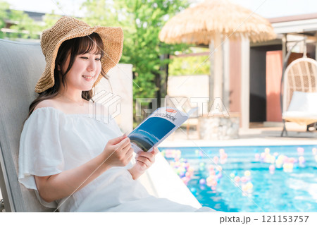 プールサイドのリクライニングチェアに座りガイドブックを読む若いアジア人女性 プールサイドのリクライニングチェアに座りガイドブックを読む若いアジア人女性 121153757