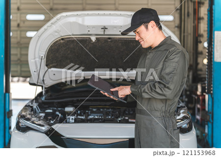 タブレットを使って自動車のエンジルームをチェックする自動車整備士の男性メカニック タブレットを使って自動車のエンジルームをチェックする自動車整備士の男性メカニック 121153968