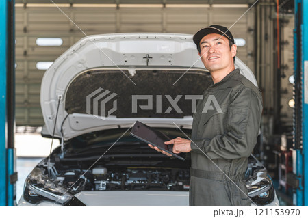 タブレットを使って自動車のエンジルームをチェックする自動車整備士の男性メカニック 121153970