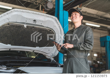 タブレットを使って自動車のエンジルームをチェックする自動車整備士の男性メカニック 121153973