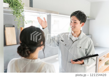 換気扇・レンジフードの説明を受ける主婦の女性と工務店・設備屋・電気工事士・業者の作業着姿の男性 121154420