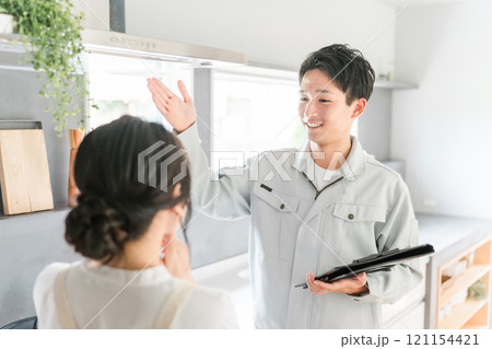 換気扇・レンジフードの説明を受ける主婦の女性と工務店・設備屋・電気工事士・業者の作業着姿の男性 121154421