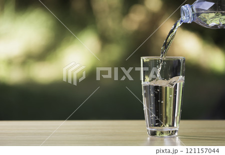 Water from plastic bottle pouring into glass on table with nature background 121157044
