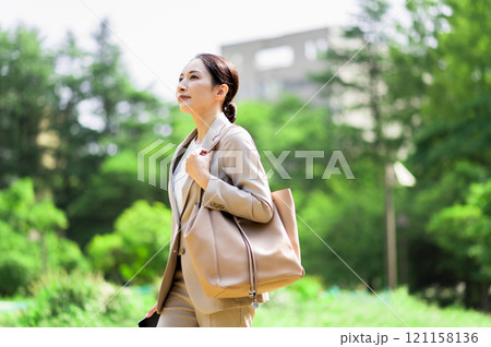 新緑の屋外を歩きながら見上げるスーツ姿の女性 121158136