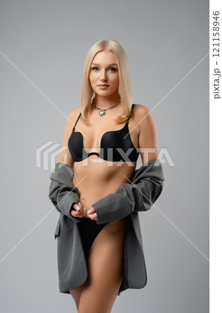 Young woman posing confidently in black lingerie and grey cardigan indoors 121158946