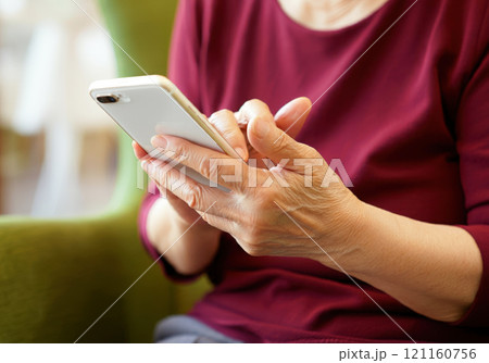 自宅のリビングでゆっくりスマホを楽しむ70代の女性 121160756