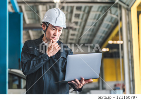 工場・倉庫・物流センターでパソコンを見ながら打ち合わせをする作業員の男性（考える・困る・悩む・調査） 121160797