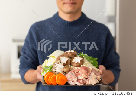 鶏の水炊き鍋の食材を持つミドル男性 121163452