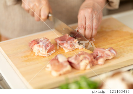 キッチンで鶏肉を切るミドル〜シニア女性の手元 121163453