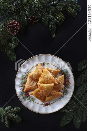 Pies with meat filling on plate. Puff pastry pies. Homemade cakes. Handmade work. Branches of nobilis or spruce, as table decoration. Flat lay. Top view. Pies with meat filling on plate. Puff pastry pies. Homemade cakes. Handmade work. Branches of nobilis or spruce, as table decoration. Flat lay. Top view. 121164530