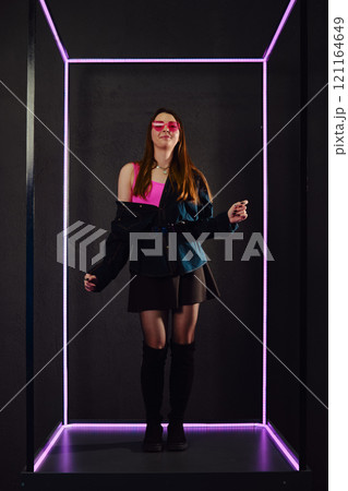 Young woman dancing in colorful lighting with stylish outfit and playful expression Young woman dancing in colorful lighting with stylish outfit and playful expression 121164649