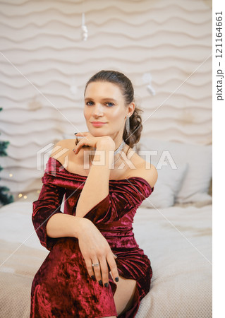 Elegant woman in a red velvet dress poses thoughtfully in a cozy interior setting Elegant woman in a red velvet dress poses thoughtfully in a cozy interior setting 121164661