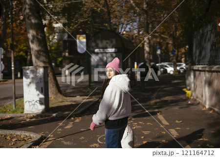 A Woman Enjoying a Leisurely Stroll in an Autumn Park While Dressed in a Cozy Outfit 121164712