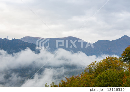 The extensive view of the lush autumn forest in the dense misty mountains creates a charming atmosphere of mystery and tranquility. Autumn in the mountains. The extensive view of the lush autumn forest in the dense misty mountains creates a charming atmosphere of mystery and tranquility. Autumn in the mountains. 121165394