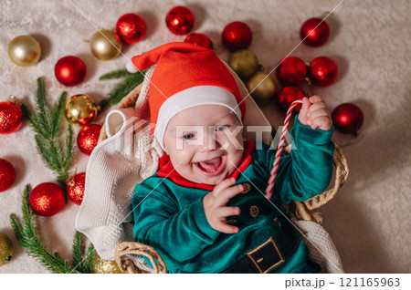 Merry Christmas and Happy New Year. A cheerful little child in a New Year's costume lies in a basket with Christmas tree balls 121165963