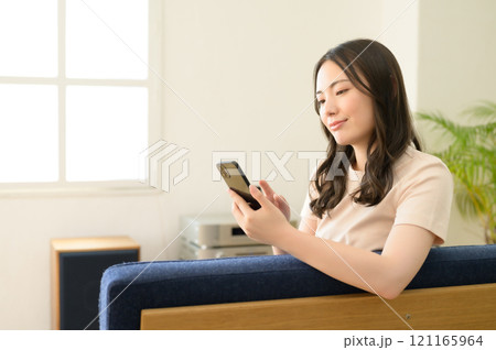 リビングのソファーに座ってスマホを見る女性 121165964