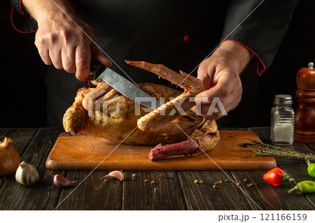 The chef expertly carves golden raw chicken surrounded by fresh herbs and vegetables, showcasing culinary skill and delicious aromas in the warm atmosphere of the restaurant kitchen The chef expertly carves golden raw chicken surrounded by fresh herbs and vegetables, showcasing culinary skill and delicious aromas in the warm atmosphere of the restaurant kitchen 121166159