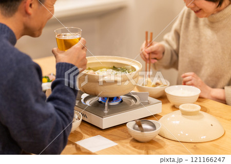 冬の夜のリビングで夕食の鍋料理を楽しむミドル夫婦 121166247