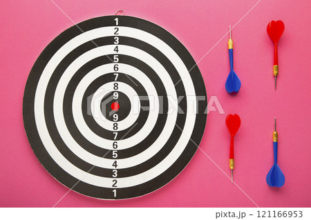 Dart board with red and blue darts on pink background. 121166953