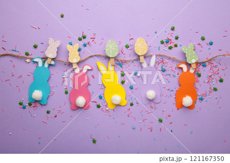 Easter rabbits handmade from colored paper on a rope with clothespins easy crafts for children on a purple background. 121167350