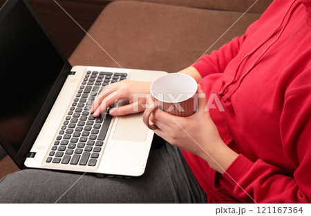 Woman sit on cozy sofa writing email on laptop and drinking coffee, girl freelancer working at computer from home, focused student studying un bed. 121167364
