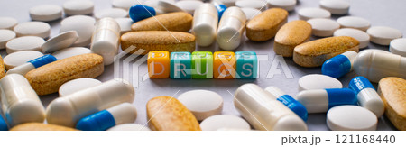 An arrangement of pills, capsules, and supplements with colorful blocks in the middle spelling out the word DRUGS 121168440