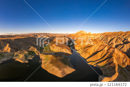 Panoramic aerial view on picturesque Azat reservoir and Eranos mountain at bright sunny evning sunset. Lake with blue water in arid area and Yeranos mountains range. Beautiful landscape. Armenia. Panoramic aerial view on picturesque Azat reservoir and Eranos mountain at bright sunny evning sunset. Lake with blue water in arid area and Yeranos mountains range. Beautiful landscape. Armenia. 121169172