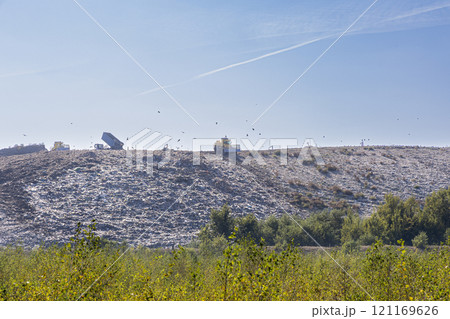 A large landfill site with garbage trucks and birds flying overhead. The image depicts the environmental impact of human waste and the need for sustainable solutions. 121169626