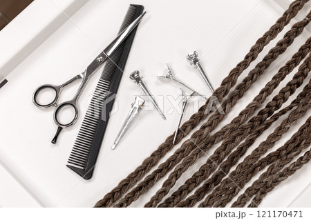 Blanks for braiding pigtails and hairdressing tools on white surface, scissors, comb, clips, close-up. Blanks for braiding pigtails and hairdressing tools on white surface, scissors, comb, clips, close-up. 121170471