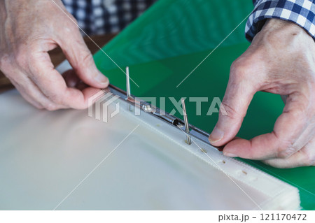 Elderly female hands with green plastic file folder, person fix files with a metal clip, close-up, selective focus. Elderly female hands with green plastic file folder, person fix files with a metal clip, close-up, selective focus. 121170472
