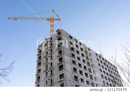 Tower cranes next to a multistory panel building under construction in the city against a blue sky. 121170479