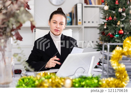 Portrait of successful business woman with New Years tinsel and Christmas tree in office 121170616