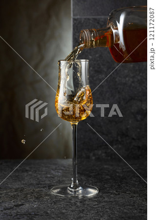 Pouring strong alcoholic drink from a bottle into a glass. 121172087