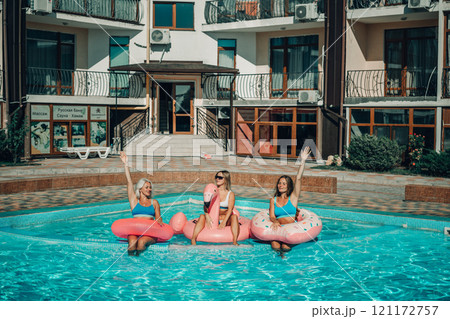 Three women are sitting on inflatable floats in a pool. Scene is lighthearted and fun. 121172757